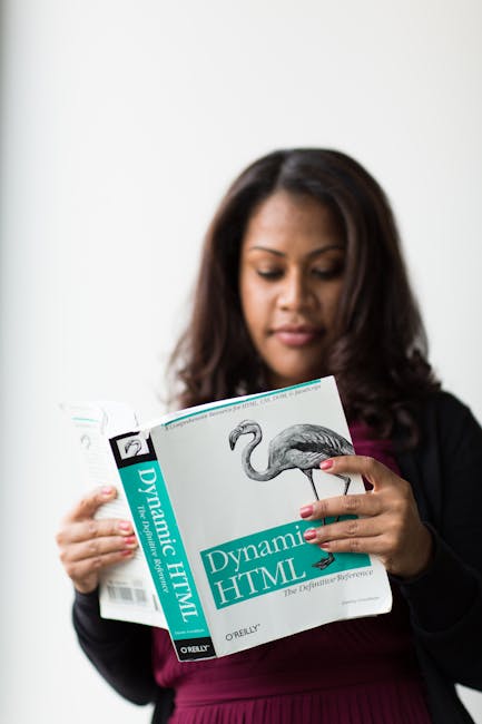 A woman with medium-length dark brown hair and light brown skin is holding an open book titled 'Dynamic HTML' printed by O'Reilly, featuring a detailed black-and-white illustration of a bird, possibly